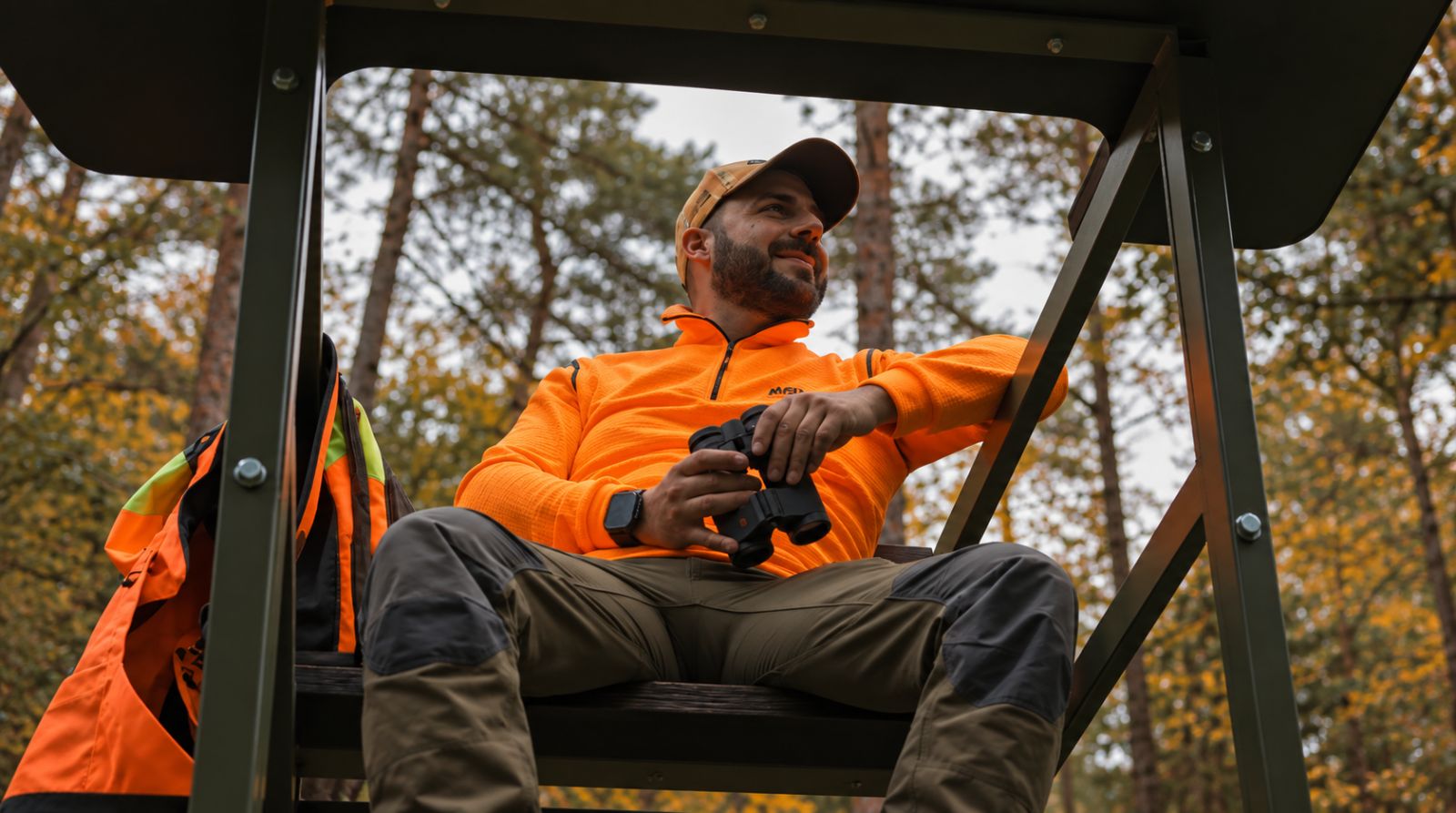 Jäger mit Fernglas auf der Sitzbank des Zauberjagd Drückjagdbocks im herbstlichen Wald