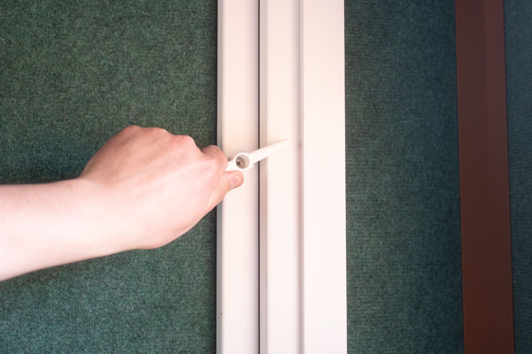 Fenstergriff im Innenraum, Wand mit grünem Filzbelag